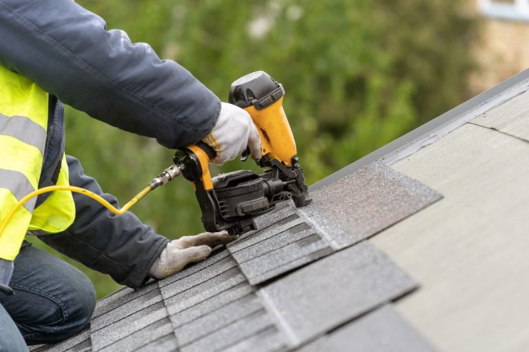 Workman using pneumatic nail gun install tile on roof of new house under construction, Shoreview